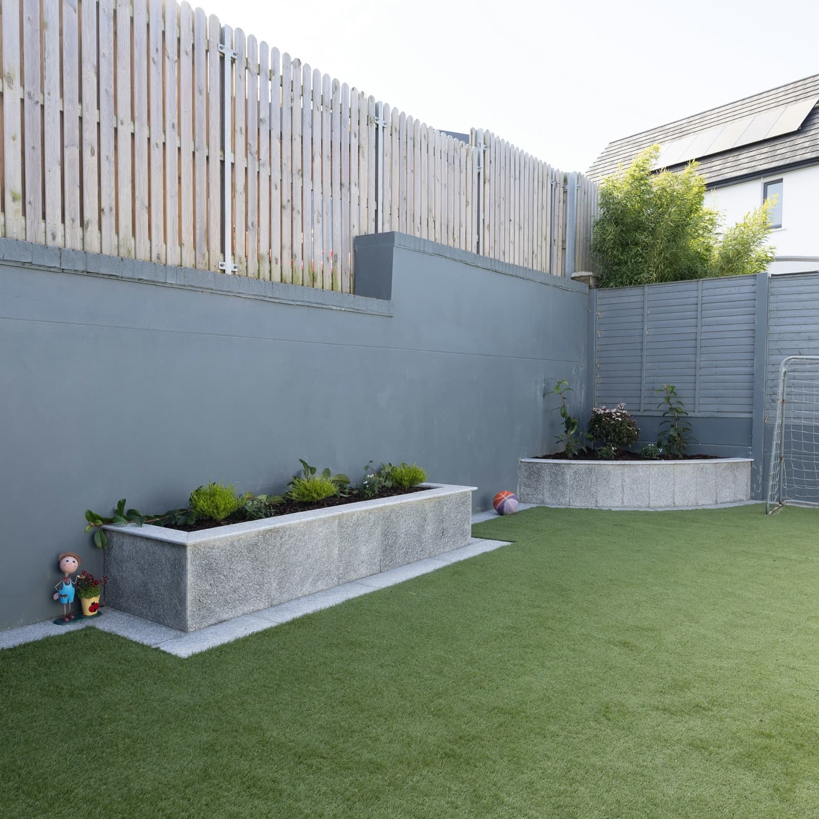 Backyard laid with artificial grass, with a kids' soccer goal, a basketball and raised garden beds